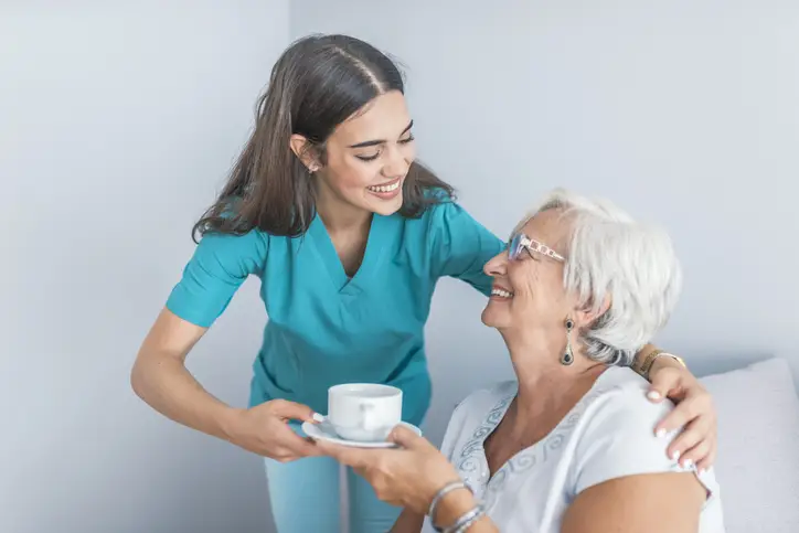 Die Pflegehelferin reicht der Klientin eine Tasse